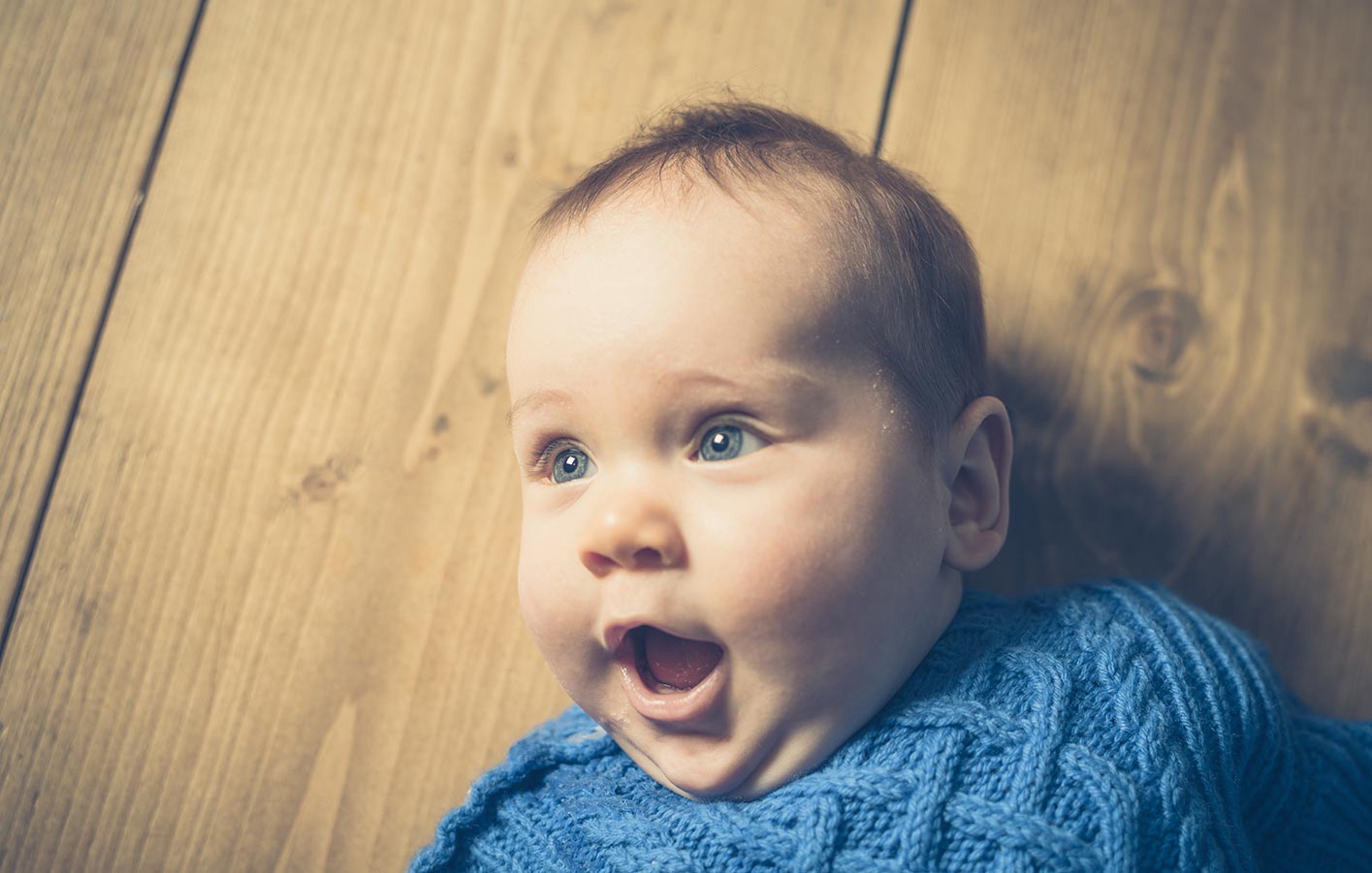 Baby liegt auf dem Parkettboden und lacht.